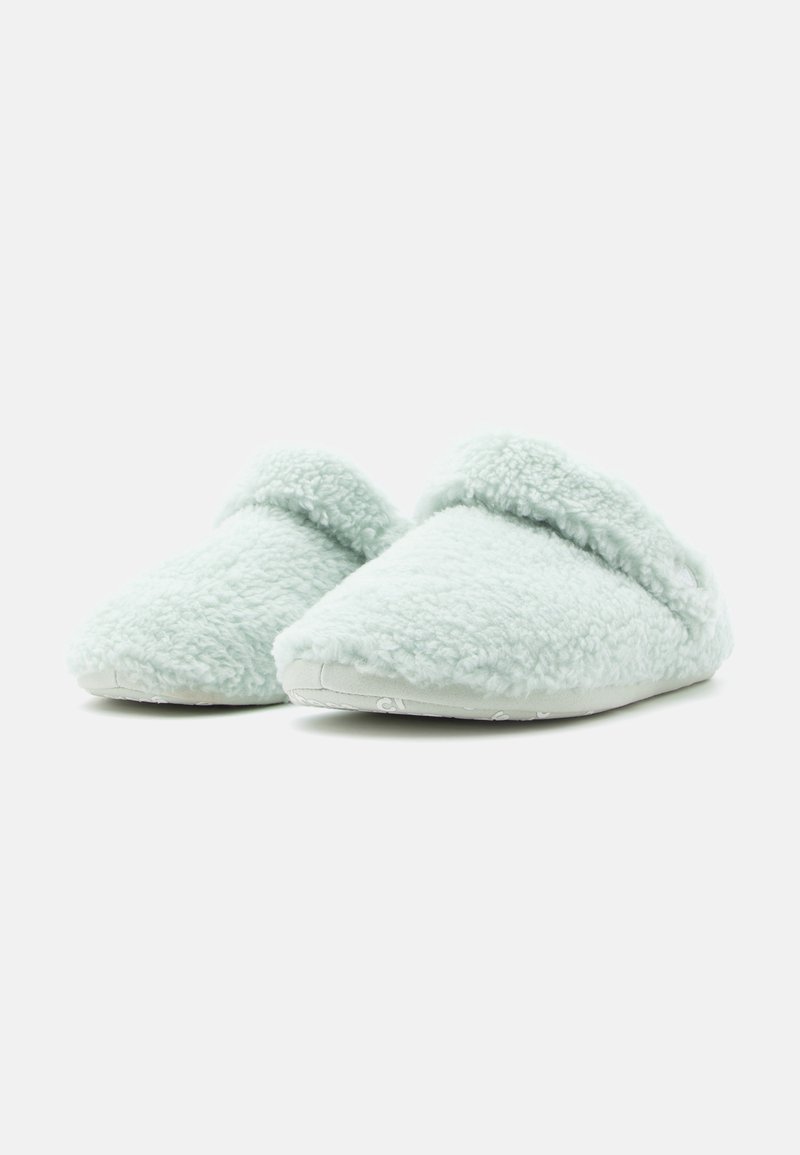 Par de pantuflas de felpa suave color azul claro con la parte delantera redondeada y puño doblado, exhibidas sobre fondo blanco.
