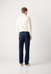 Cream sweater with long sleeves, paired with navy trousers. Smooth texture, relaxed fit. Trousers feature back pockets and straight leg design.