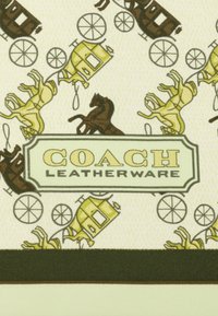 Materiał w wzory z żółtymi powozami i brązowymi końmi. Centralna etykieta brzmi "COACH LEATHERWARE." Tło jest jasnobeżowe z teksturą.