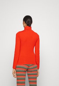 Röd långärmad polokrage-topp med en figursydd design, gjord av ett mjukt material. Har en hög krage och slät textur för komfort.