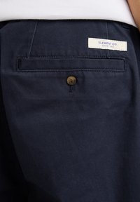 Navy blue cotton pants with a back pocket featuring a brown button and a white label that reads "ELEMENT CO. SINCE 1992." Smooth texture.