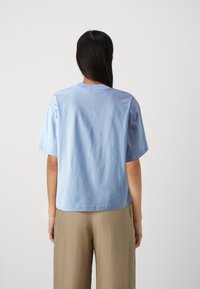 Ljusblå kortärmad bomullströja med rund hals, avslappnad passform och slät yta, tillsammans med beige vida byxor.