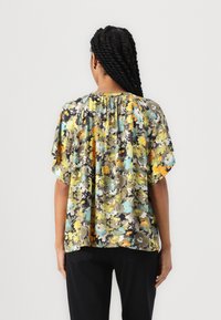 Bluse med blomstertrykk som har korte ermer, gule, blå og oransje detaljer på en mørk bakgrunn, med samlet bakdetalj.