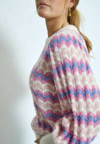 Luchtig gebreid trui met een zigzagpatroon in roze, blauw en crème, met een losse pasvorm en ronde halslijn. De stof heeft een zachte textuur.
