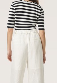 Top rigato bianco e nero a coste con maniche tre quarti, abbinato a pantaloni bianchi a vita alta e gamba larga con cintura elastica.