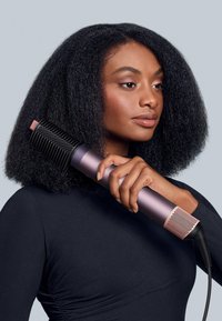 Hårtork med en cylindrisk, metallisk kropp i gradientnyanser av lila och rosa, med en texturerad svart munstycke och en elektrisk sladd.