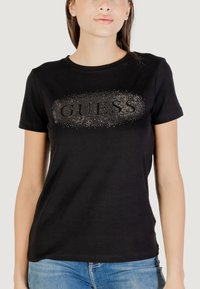 T-shirt in cotone nero con scollatura rotonda e maniche corte. La parte anteriore presenta "GUESS" decorato con applicazioni in strass.