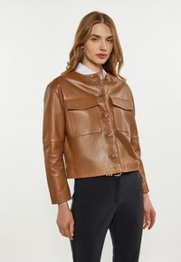 Braune Lederjacke mit verkürztem Design, ausgestattet mit zwei Brusttaschen und einem Knopfverschluss. Glatte Textur und Stehkragen.