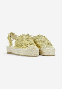 Espadrilles de oro tejidas con un diseño texturizado, lados recortados y suelas de plataforma de yute. Las correas ajustables en el tobillo completan el estilo.