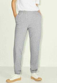 Grå mjukisbyxor med elastisk midja, sidofickor och tapered-ben-design, tillsammans med vita sneakers på en ljus bakgrund.