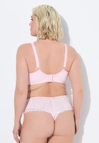 Sujetador rosa claro con tirantes ajustables y cierre de gancho, combinado con bragas hipster de encaje a juego que presentan detalles de encaje floral.