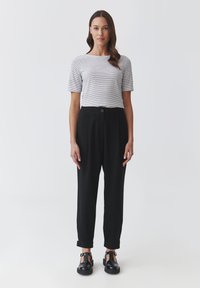 Gestreept T-shirt met korte mouwen, gecombineerd met hoge zwarte broeken. De broeken hebben een knoopsluiting en een opgerolde zoom. Zwarte schoenen maken de outfit compleet.