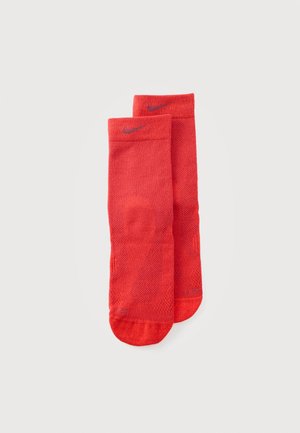 Un par de calcetines Nike de media caña de color rojo intenso, con paneles de punto texturizado y logotipos Swoosh, sobre un fondo liso y claro.