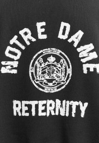 Κείμενο Notre Dame πάνω από έναν κυκλικό θυρεό με φιγούρες και κορώνα, και η λέξη "RETERNITY" με έντονα γράμματα κάτω σε μαύρο ύφασμα.