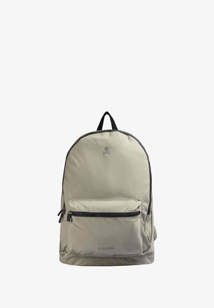 Mochila gris claro con forma redondeada, cremalleras negras y un bolsillo frontal. Presenta un logo en la parte superior y una textura de tela duradera.