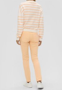 Ein hellrosa und weiß gestreifter Pullover, kombiniert mit pfirsichfarbenen Skinny-Jeans. Die Jeans haben Gesäßtaschen und werden von weißen Sneakers ergänzt.
