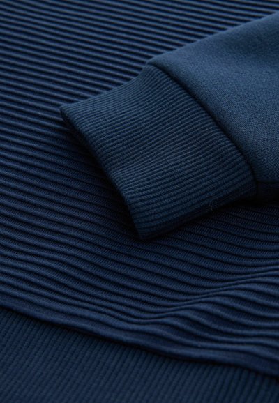 Tessuto azzurro navy con texture e motivi a costine orizzontali, dotato di un elegante dettaglio ai polsini. Materiale morbido e elastico, ideale per l'abbigliamento casual.