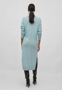 Ljusblå, lång stickad klänning med hög krage, ribbad mudd och sidofickor, bärs över knähöga svarta stövlar.