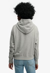 Lysegrå hættetrøje med en stor hætte, ribstrikkede ærmeafslutninger og kant. Blødt stof med en afslappet pasform, båret over blå denimjeans.