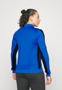 Blauw sportief langemouwen shirt met zwarte zijpanelen, een hoge kraag en een slim fit ontwerp. Smooth textuur, lichtgewicht stof.