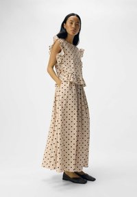 Vestido de lunares en tela rosa pálido, con mangas rizadas, cintura ajustada, detalle de peplum y falda fluida. Bailarinas negras completan el look.
