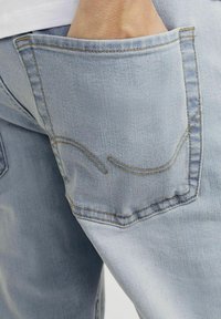 Jeans en denim bleu clair avec une poche arrière dotée d'une couture incurvée distinctive. Le tissu semble doux avec une texture lisse.