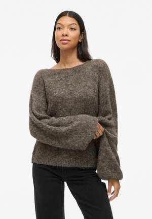 Pull en tricot marron avec des manches larges, coupe ample et texture douce. Présente un col bateau et est associé à un pantalon noir.
