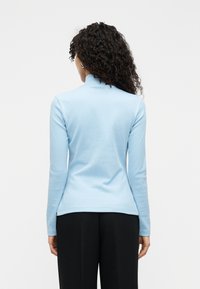 Ανοιχτό μπλε μπλούζα με μακριά μανίκια και ψηλό λαιμό, με λεία υφή και εφαρμοστή σχεδίαση. Η πίσω όψη δείχνει μια απλή, καθαρή σιλουέτα.