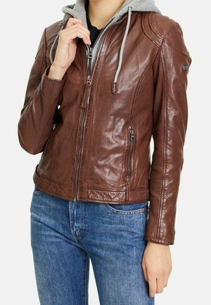 Henkilö vetämässä vetoketjua kiinni ruskeassa nahkatakissa, joka on pukeutunut harmaan hupparin päälle, yllään siniset farkut, kuva keskivartalosta kaulaan asti.