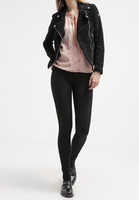 Černá semišová motorkářská bunda, světle růžová saténová halenka s krajkovými detaily, černé legíny a černé boty s přezkovými akcenty.