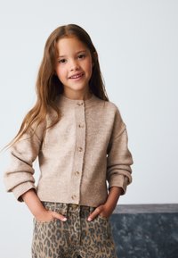 Bézs kardigán kerek nyakkivágással, gombos záródással és bordázott mandzsettákkal; leopárdmintás farmerrel, oldalzsebekkel párosítva.