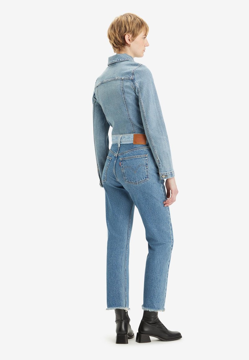 Lichtblauwe spijkerjas met een getailleerd ontwerp, knopen aan de voorkant en lange mouwen, gecombineerd met hooggewaardeerde taps toelopende jeans en zwarte enkelboots.