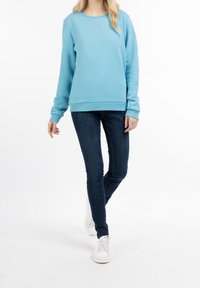 Ljusblå bomullströja med långa ärmar och rund halsringning, tillsammans med mörka jeans och vita sneakers. Enkel, slät textur.