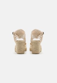 Beige wedge sandals with a woven fabric upper, featuring a rounded back, open heel, and textured espadrille-style sole.