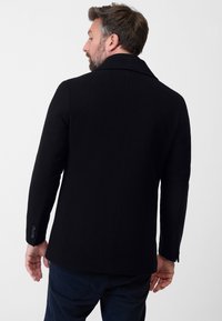 Zwarte wolmix jas met een inkeping kraag, getailleerde pasvorm, enkele knoopdetail op de mouw en een gladde textuur. Zichtbare achternaad.