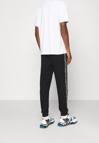 Witte korte mouwen t-shirt gecombineerd met zwarte joggingsbroek met witte zijaccenten, afgewerkt met gekleurde sportschoenen.