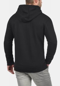 Sudadera negra con capucha ajustable, puños y dobladillo acanalados, textura de tela suave y diseño ajustado. La vista trasera muestra una construcción sin costuras.