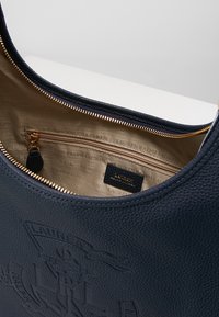 Marinblå läderhandväska med en texturerad utsida, guldfärgade detaljer och ett fack med dragkedja på insidan med beigemönstrad foder.