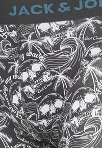 Mutande in tessuto nero con un motivo di teschi e palme bianchi, accompagnate da testi decorativi. Vita elasticizzata di colore grigio scuro con il logo "JACK & JONES".