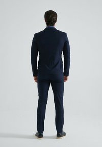Costume marine avec une silhouette ajustée et des revers crantés. Pantalons sur mesure et chaussures noires avec une semelle légère. Texturé de tissu lisse.