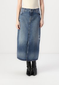 Denim maksi krilo v srednje modri barvi z sprednjim gumbom, subtilnim zbledeljem in pohabljeno obrobo. V kombinaciji z črnimi gležnjarji.