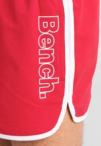 Rote Schwimmshorts mit einem weißen Logo "Bench." auf der linken Seite, weißem Saum und kontrastierenden weißen Nähten.