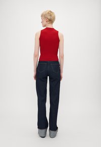 Rød ribbet ermeløs topp kombinert med mørkeblå flagrende jeans. Jeansene har et klassisk fem-lomme-design og diskret søm.