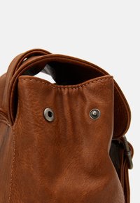 Bruine leren tas met een afgeronde bovenkant, voorzien van zilveren drukknoophardware en gestikte details. Zachte, gestructureerde afwerking met een licht versleten uitstraling.