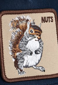 Gestickter Aufnäher mit einem grauen Eichhörnchen und buschigem Schwanz auf beigem Stoff. Der Text lautet "NÜSSE" und ist von braunem Stich umrandet.