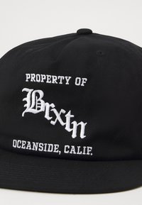 Black cap with white embroidered text stating "PROPERTY OF Brixton OCEANSIDE, CALIF." Structured design with a flat brim.