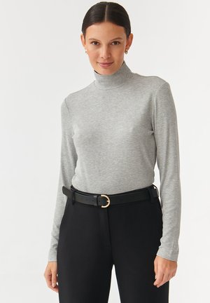 Light gray ribbed turtleneck made from a soft, stretchy fabric, paired with black high-waisted trousers and a black belt featuring a gold buckle.