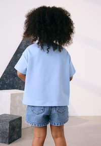 T-shirt bleu clair à manches courtes avec une coupe décontractée, assorti à un short en denim. Tissu doux, design simple avec manches retroussées.