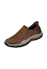 Zapato marrón tipo slip-on hecho de cuero y materiales sintéticos. Cuenta con una suela de goma, acentos oscuros contrastantes y detalles de costura.