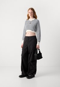 Crop top i hvit og marineblå striper, høyt liv svarte cargo-bukser og svarte tykke sko. Tilbehøret inkluderer en liten svart håndveske.